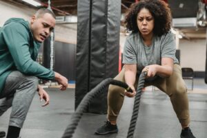 women/ man personal trainer and trainee battle ropes
